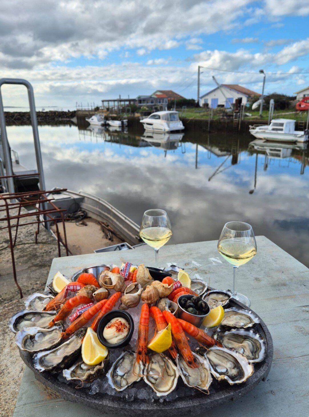 Deux verres de vin blanc et un plateau de fruits de mer sur une table face au port ostréicole