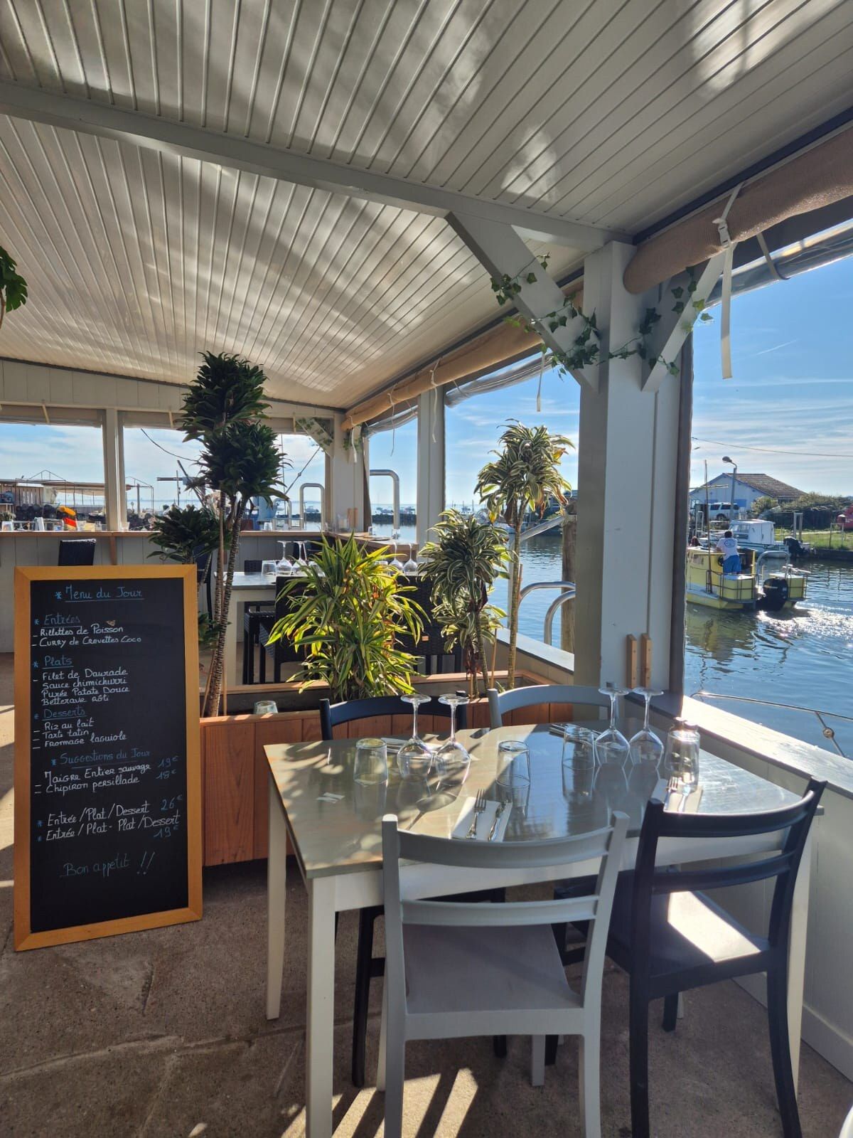 Salle vitrée de la cabane ouverte sur le port, avec l'ardoise du jour